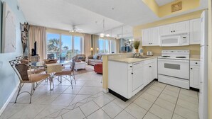 A modern kitchen with white cabinets, a microwave, and a stove. There is a dining area with a table and chairs.