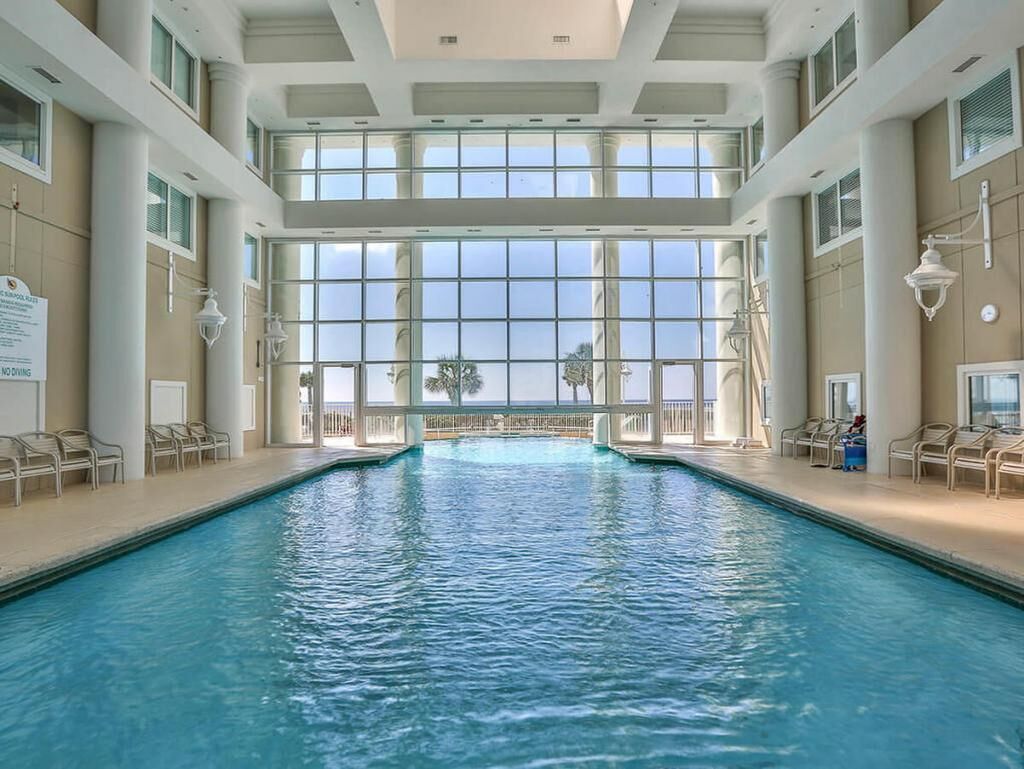 An indoor swimming pool with clear views through large windows, surrounded by lounge chairs.