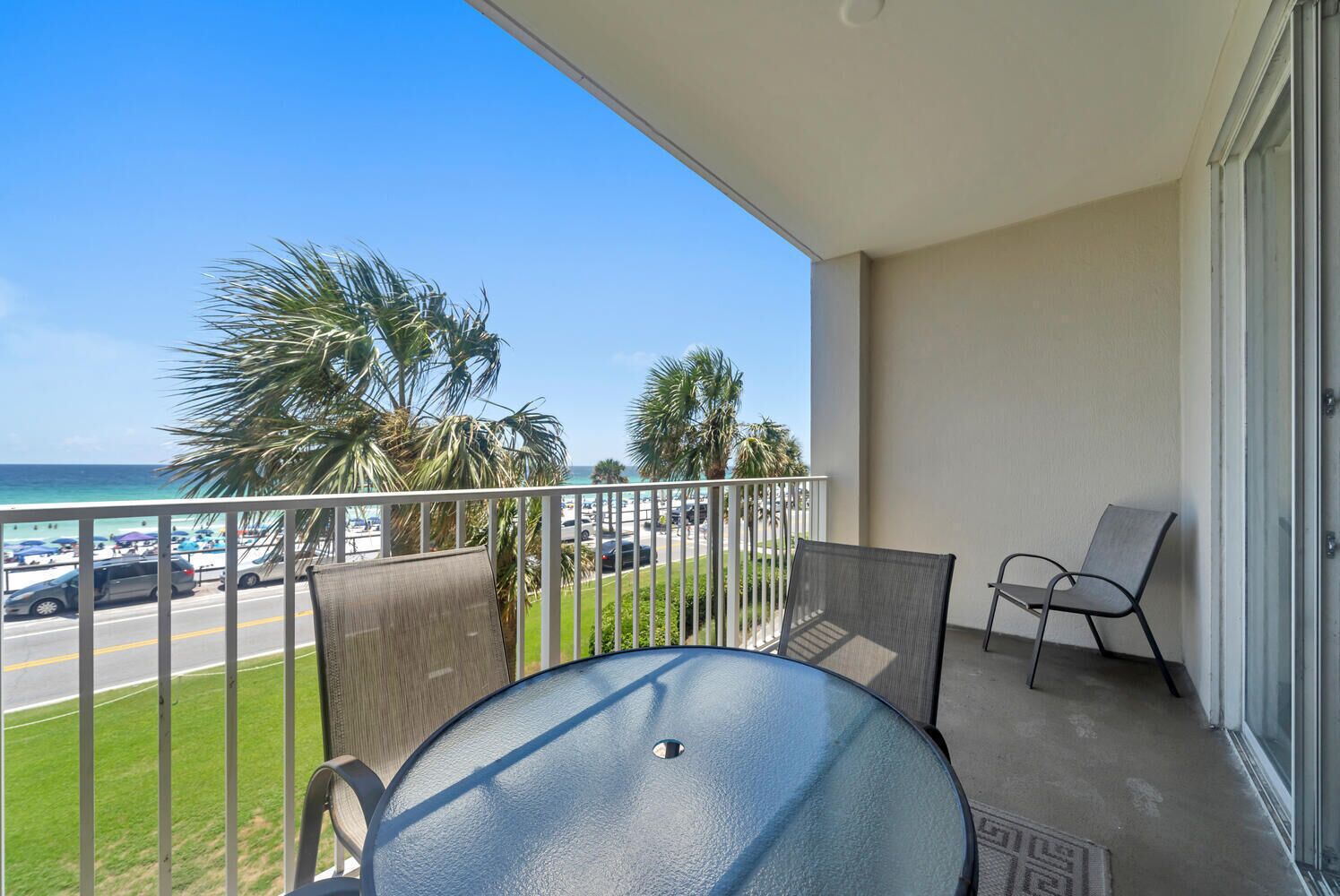 A balcony with a table and chairs, overlooking a beach with palm trees and a view of the ocean.