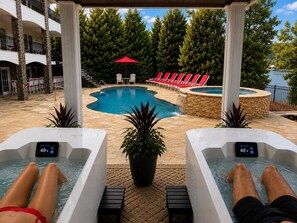 Un área de piscina con dos jacuzzis, sillas de descanso y vistas a un lago.