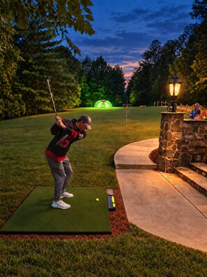 A person on a green mat at a golf course, a lamp post, and a stone wall.