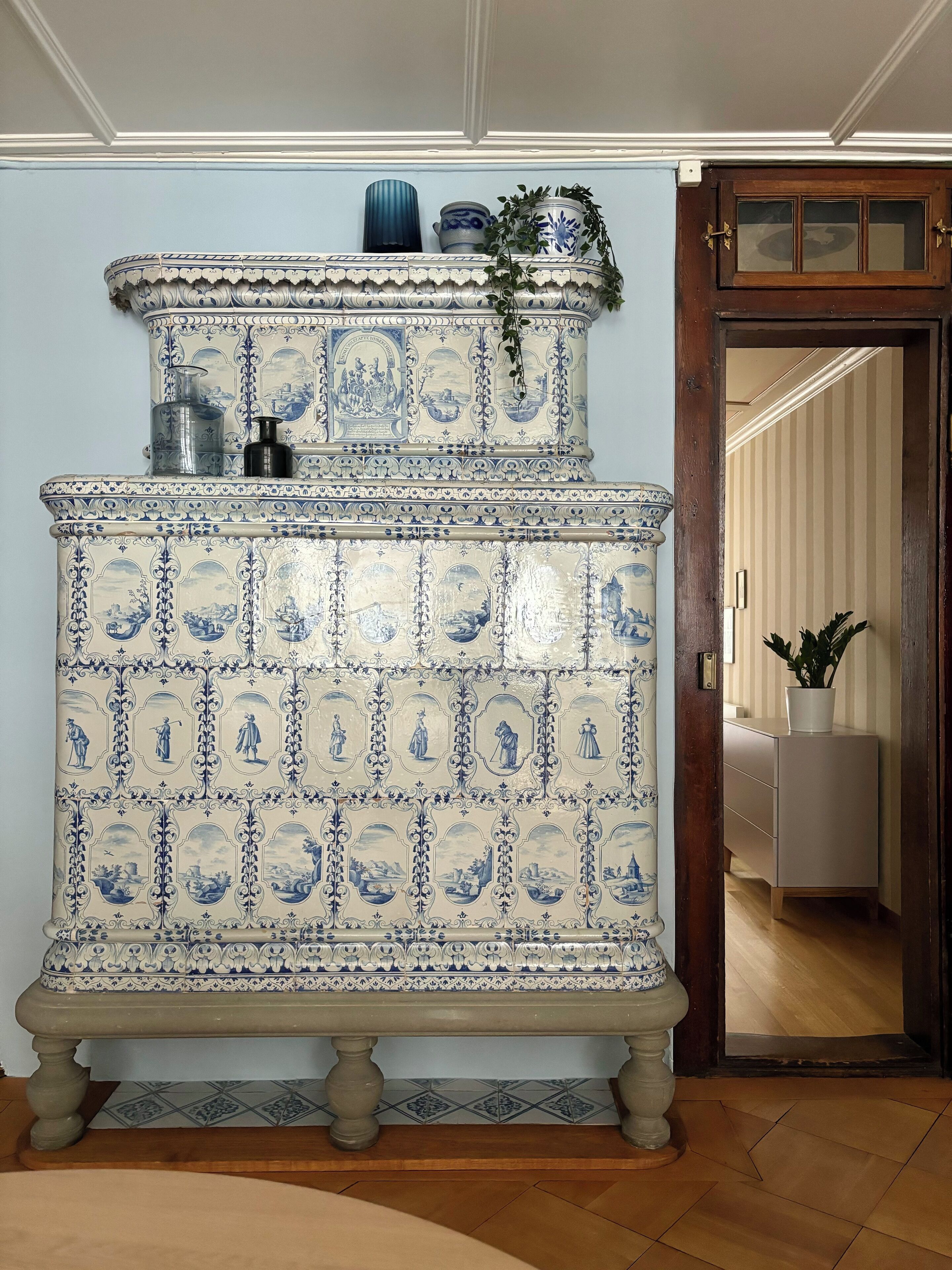 Un buffet traditionnel aux carreaux bleus et blancs, surmonté d’un élément décoratif, placé dans une pièce dotée d’une porte en bois et donnant sur une autre pièce.