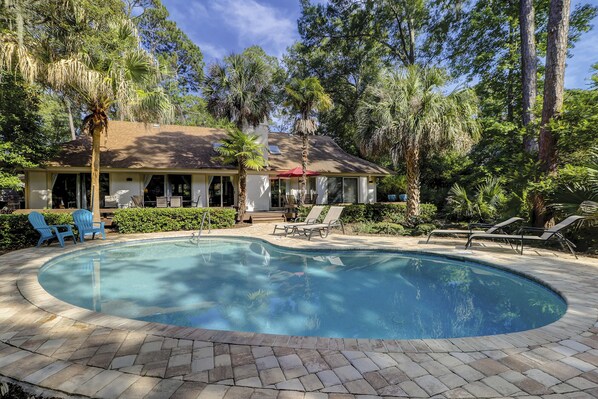 A pool area with lounge chairs, a house with a patio, and surrounding trees. - 67 Mooring Buoy- Pet Friendly & and only a Quick 3-Minute Walk to the Beach (Hilton Head Island)