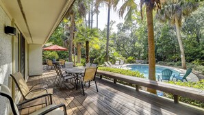 Terraza de madera con mobiliario exterior, piscina y vegetación tropical.