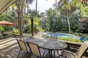A poolside area with a round table and chairs, surrounded by lush greenery and a swimming pool. - 67 Mooring Buoy- Pet Friendly & and only a Quick 3-Minute Walk to the Beach (Hilton Head Island)