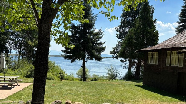 Une propriété au bord du lac, dotée d’une table de pique-nique, d’un bâtiment en pierre et d’une zone herbeuse parsemée de rochers.