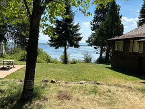 A lakeside property with a picnic table, a stone building, and a grassy area with rocks.