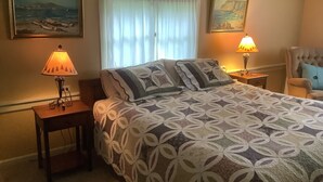 Une chambre à coucher avec un lit, deux tables de chevet avec des lampes, une chaise et deux tableaux encadrés accrochés au mur.