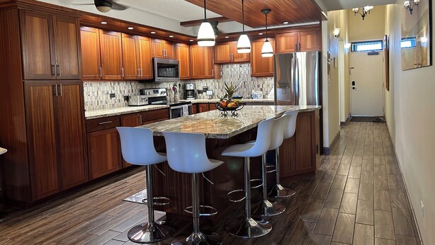 Una cocina moderna con armarios de madera, electrodomésticos de acero inoxidable y una isla central con taburetes de bar.