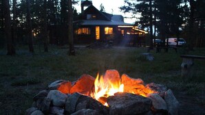 A stone fire pit in a forested area with a lodge in the background. - Large home on 5 acres, 5 bedrooms, 3 bathrooms and sleeps up to 14 people (Fraser)