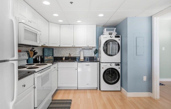 A compact kitchen with white cabinets, a microwave, a stove, and stacked washing machines. - Amazing Panoramic Views of OC From This Beautiful 2BR 2BA Oceanfront Unit! (Ocean City)