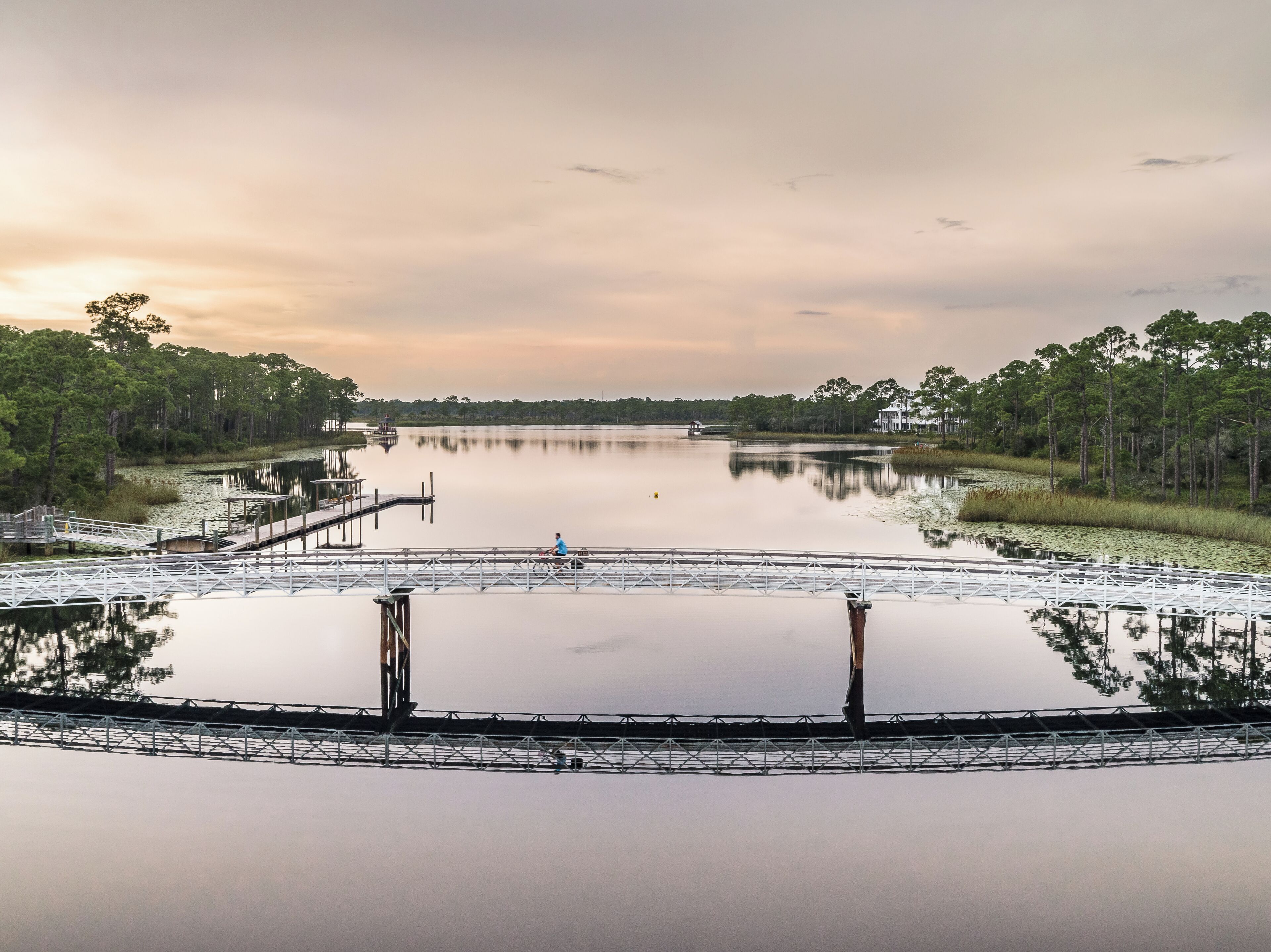 A calm lake with a dock and a pedestrian bridge.