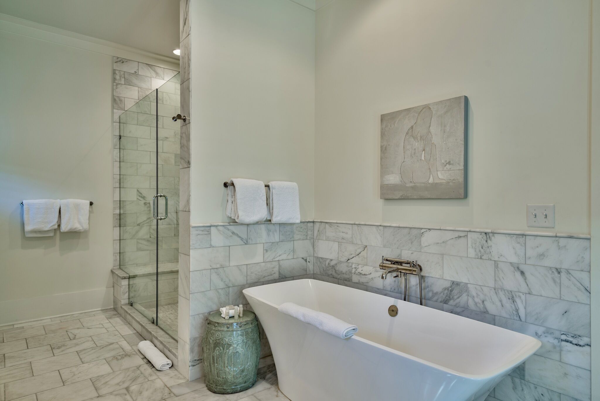 A modern bathroom with a glass-enclosed shower, a freestanding bathtub, and marble-tiled walls.