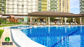 A swimming pool with lounge chairs and a covered area, surrounded by high-rise residential buildings. - Brand New Condo (Fully Furnished) with Fast WIFI & Cable TV (Unknown)