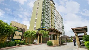 A multi-story residential building with a green and beige facade, a gated entrance, and a sign indicating a community. - Brand New Condo (Fully Furnished) with Fast WIFI & Cable TV (Unknown)