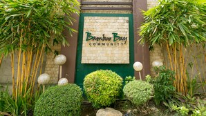 A sign for Bamboo Bay Community with a brick wall and green door, surrounded by various plants and a rock. - Brand New Condo (Fully Furnished) with Fast WIFI & Cable TV (Unknown)