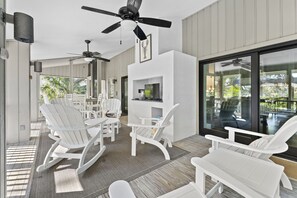 A covered outdoor seating area with white chairs and tables, ceiling fans, and a TV mounted on a wall. - Pelican's Perch – 4th Row Sea Pines Home, Pool, Free Seasonal Heat, 800 Ft to Beach (Hilton Head Island)