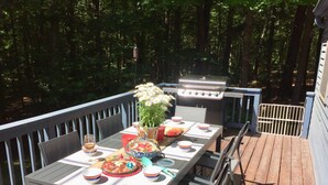 An outdoor deck with a dining table set for a meal, surrounded by chairs, and a barbecue grill. - <br>Escape to our incredibly private home on 30 acres! (Saugerties)