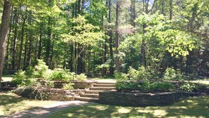 A stone staircase leading up to a stone wall, surrounded by lush greenery and tall trees. - <br>Escape to our incredibly private home on 30 acres! (Saugerties)