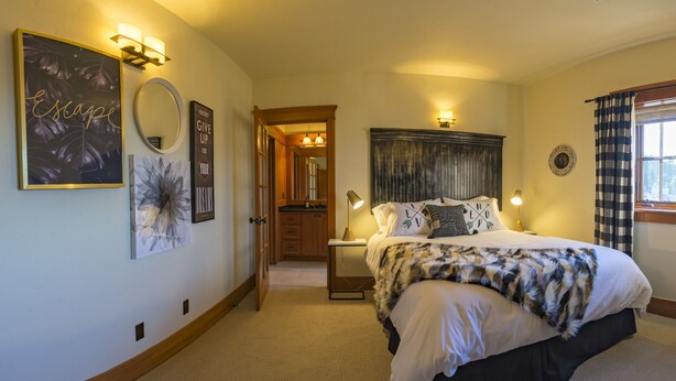 A bedroom with a bed, bedside lamps, a mirror, artwork, and a window with curtains. - FisherBros flats 203 (Astoria)