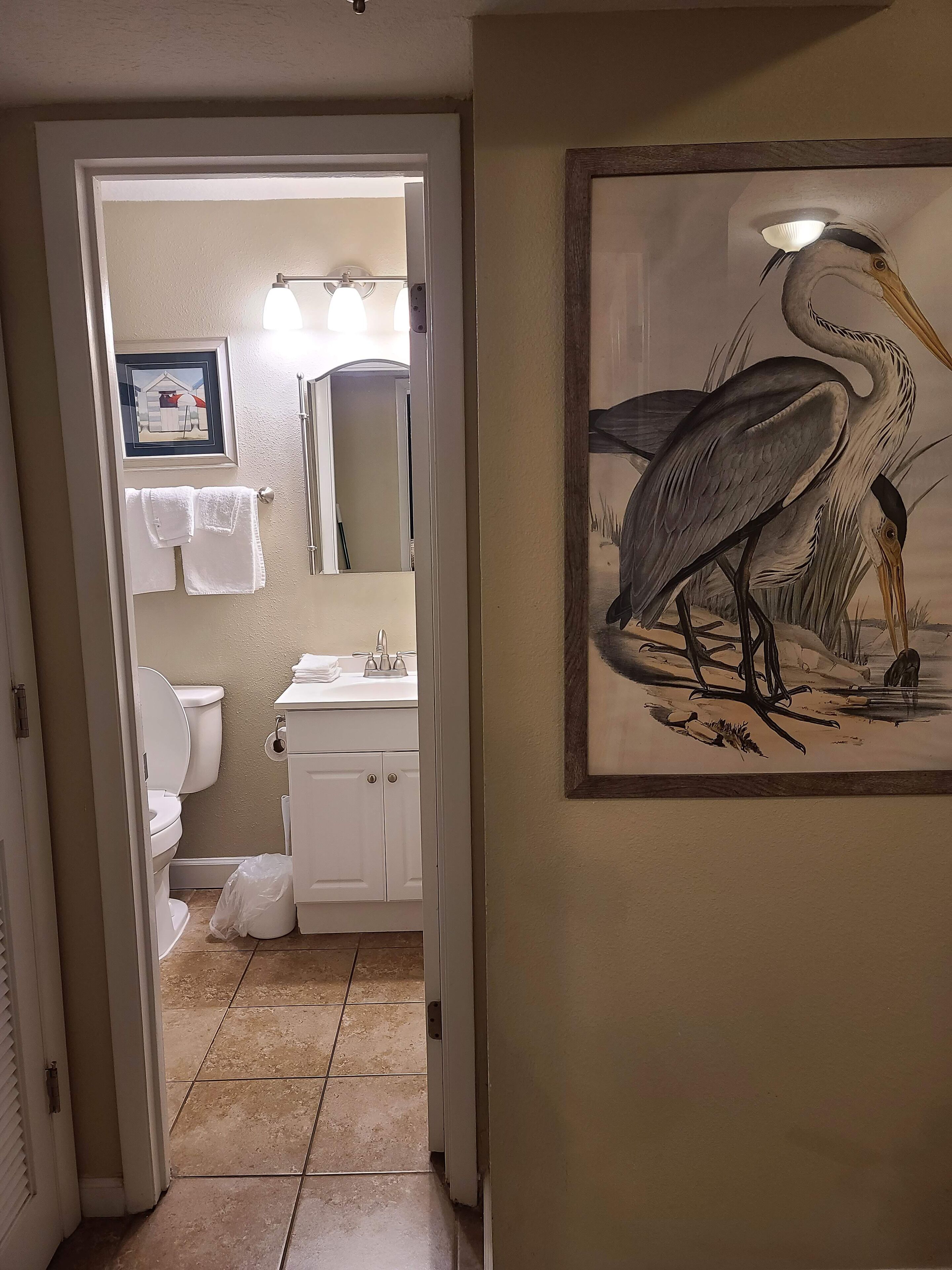 Une salle de bain équipée de toilettes, d’un lavabo et d’un porte-serviettes. Un tableau représentant un oiseau est accroché au mur.