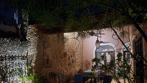 Eine rustikale Terrasse im Freien mit einer Steinmauer, einem Metallgitter und einem Tisch mit Stühlen.