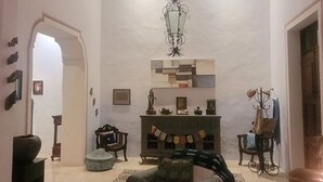 Ein großzügiges Wohnzimmer mit hohen Decken, einem imposanten Kronleuchter und einem Kamin. Mehrere Sitzgruppen und ein Couchtisch befinden sich in der Mitte.