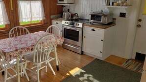 A kitchen with wooden cabinets, a stove, a microwave, and a dining table with chairs. - Point Robinson Lighthouse - Keeper's Quarters B (Vashon Island)