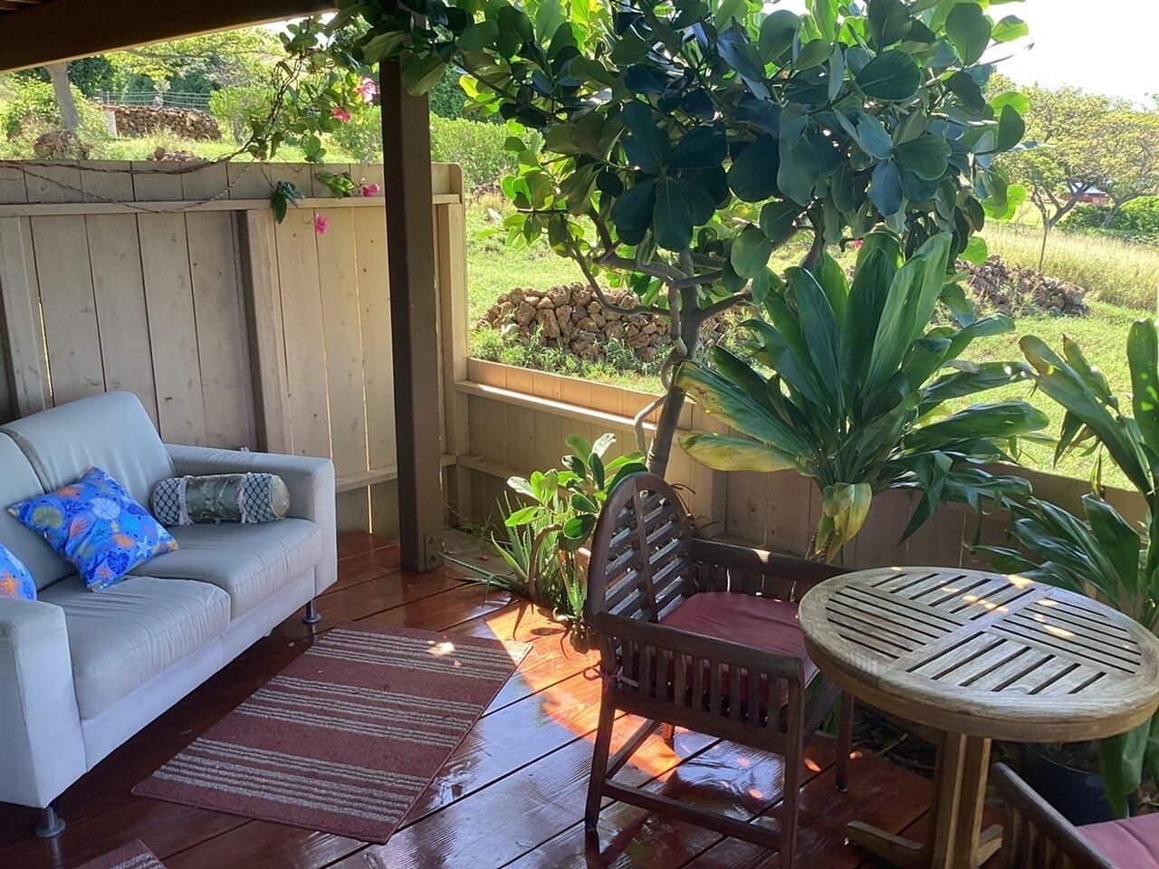 Un patio techado con un sofá, una silla de madera y una mesita.