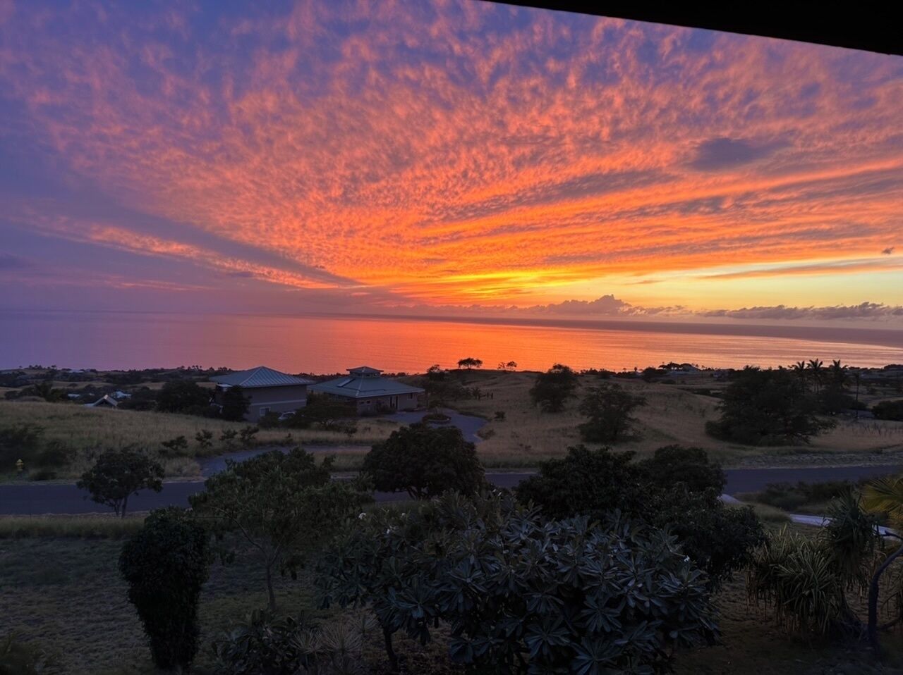 A sunset over a coastal landscape with houses and vegetation.