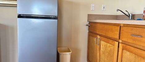 Une cuisine compacte dotée d’un réfrigérateur encastré, de meubles de rangement en bois, d’une petite poubelle et d’un plan de travail avec un évier.