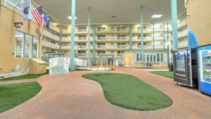 A multi-level hotel atrium with a central walkway, artificial grass, vending machines, and flags. - Walk to beach, indoor/outdoor pools, washer/dryer (Hilton Head Island)
