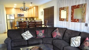 A living room with a sectional sofa, a coffee table, and a kitchen in the background. - Courchevel 27 (Mammoth Lakes)