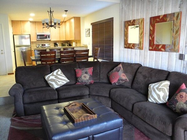 A living room with a sectional sofa, a coffee table, and a kitchen in the background.
