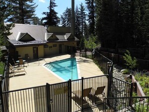 A pool area with lounge chairs, a building with a sloped roof, and a forested background.