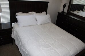 Een bed met witte beddengoed, een donker hoofdbord en een dressoir met lades.