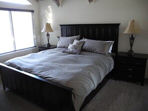A bedroom with a large bed, two bedside tables, and a window with blinds.