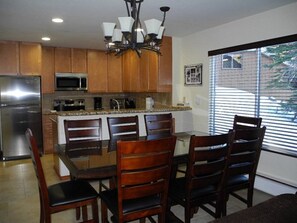 A modern kitchen with wooden cabinets, a stainless steel refrigerator, a microwave, and a chandelier.