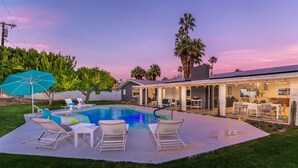 Un patio trasero con piscina, sillas de descanso y una zona de estar.