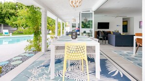 Un comedor interior con vista a la piscina, mesa blanca, silla amarilla y decoración moderna.