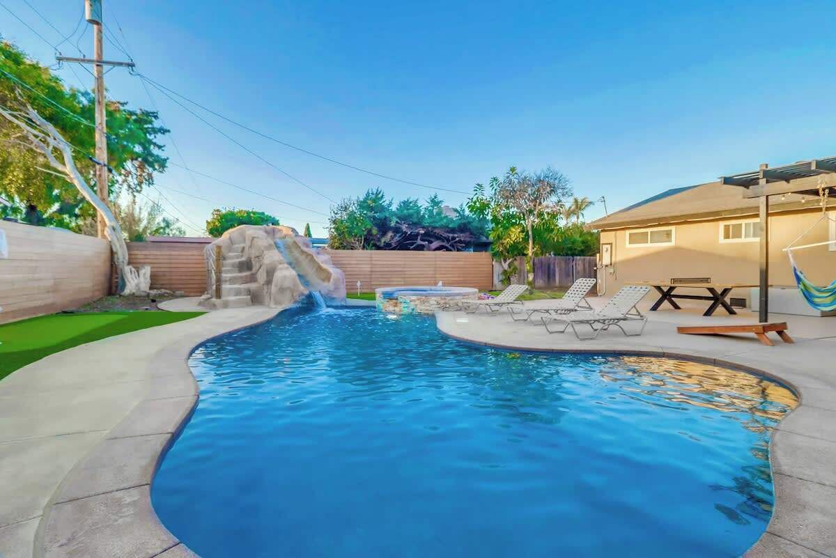 A backyard with a swimming pool, a waterfall feature, and lounge chairs.