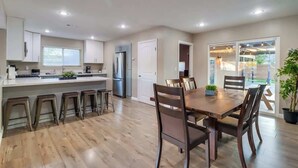 A modern kitchen with a central island, bar stools, a dining table with chairs, and a refrigerator. - Salt Water Pool & Mini Golf - Close to Downtown (Bonita)