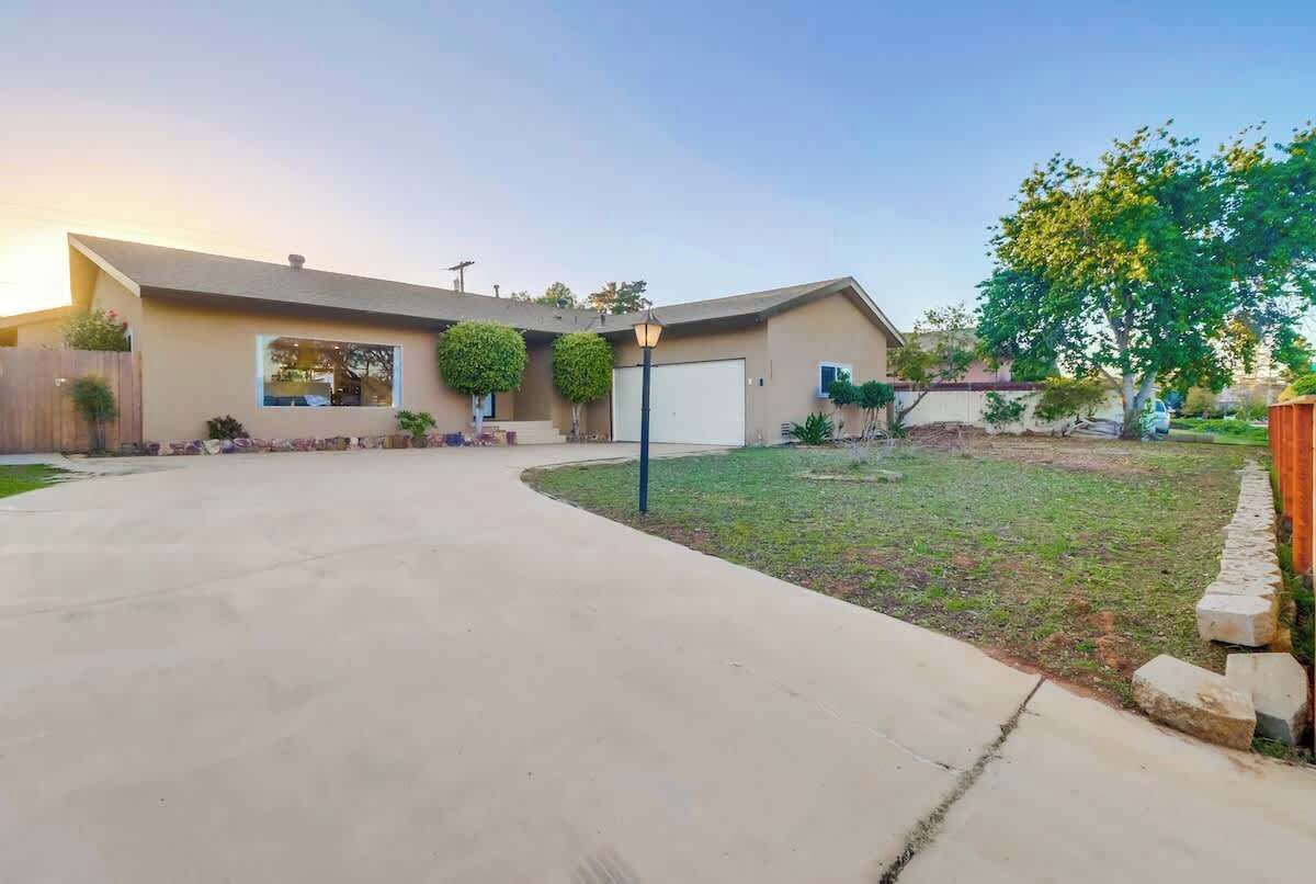 A single-story house with a garage, a front yard with a lawn and a tree, and a curved driveway.