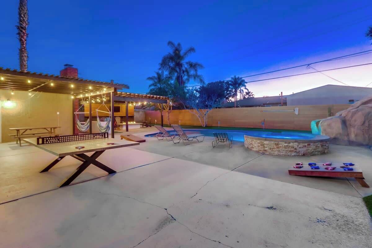 A backyard with a pool, lounge chairs, a table, and string lights.