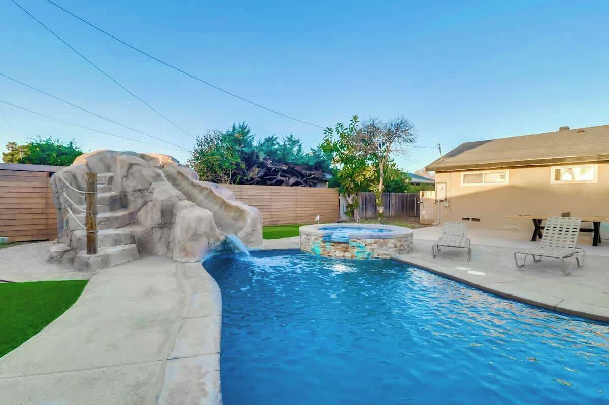 A backyard with a swimming pool, a hot tub, and a rock waterfall feature.