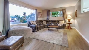 A living room with a sectional sofa, a round coffee table, and a view of the outside. - Salt Water Pool & Mini Golf - Close to Downtown (Bonita)