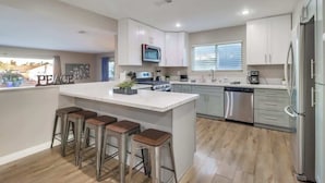 A modern kitchen with a central island, stainless steel appliances, and bar stools. - Salt Water Pool & Mini Golf - Close to Downtown (Bonita)
