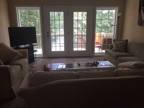A living room with a flat-screen TV, two couches, a coffee table with gaming controllers, and a sliding glass door leading to an outdoor patio. - Secluded Seneca/Clemson Lake Hartwell Waterfront, 3 miles to CU (Seneca)