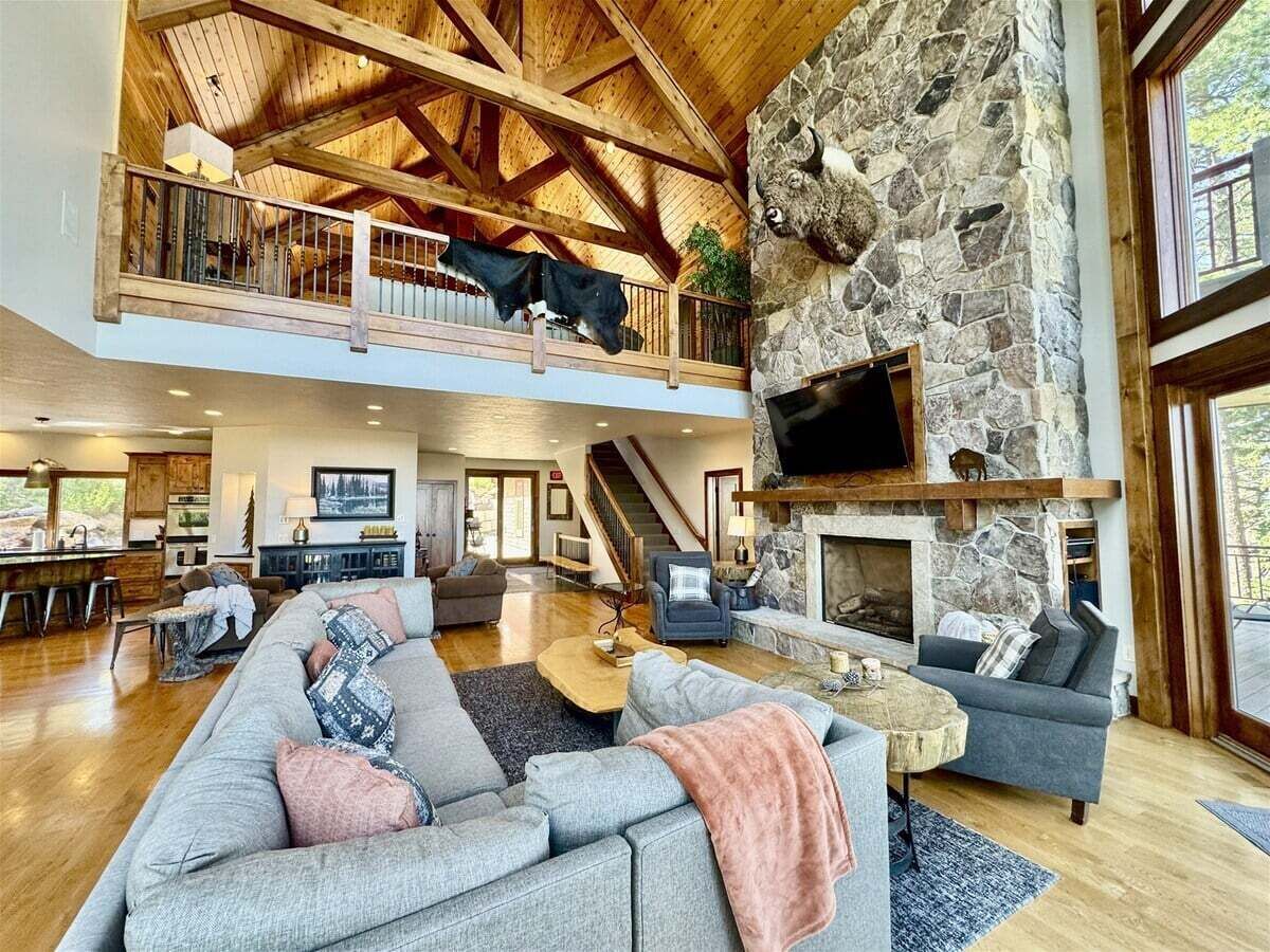 A spacious living area with a stone fireplace, a large gray sofa, and a wooden ceiling.