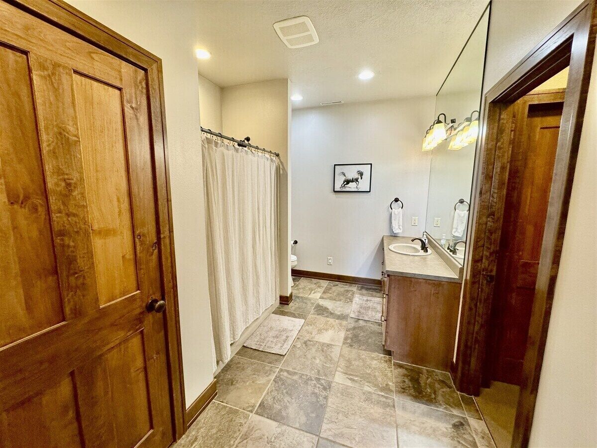 A bathroom with a wooden door, a shower curtain, a sink, a mirror, and a framed picture on the wall.